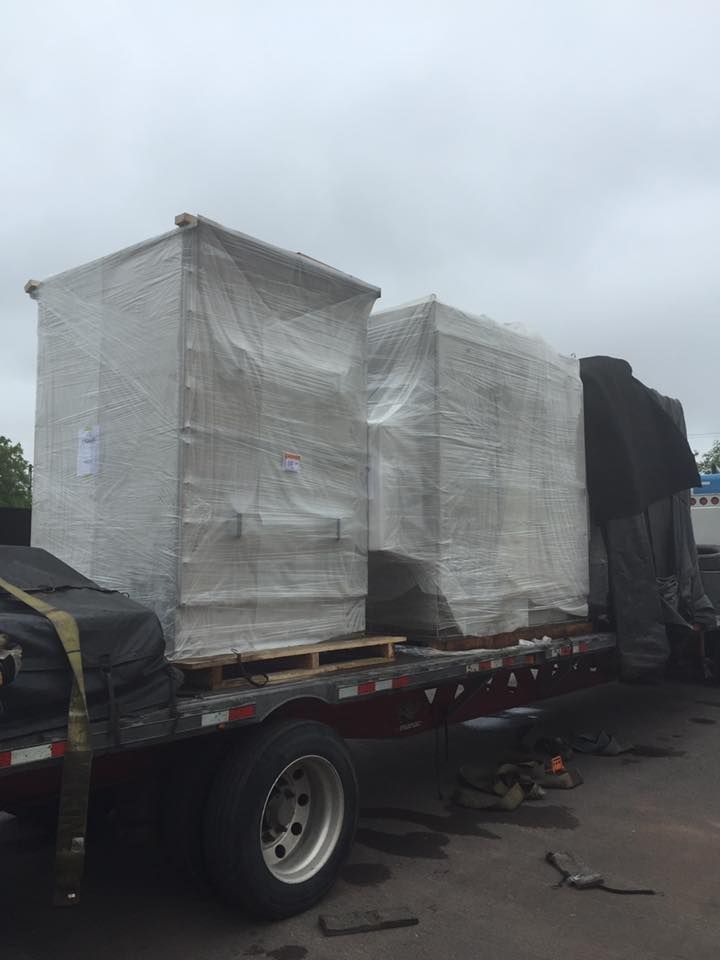 Two large, shrink-wrapped industrial crates secured on the flatbed of a semi-trailer outdoors.