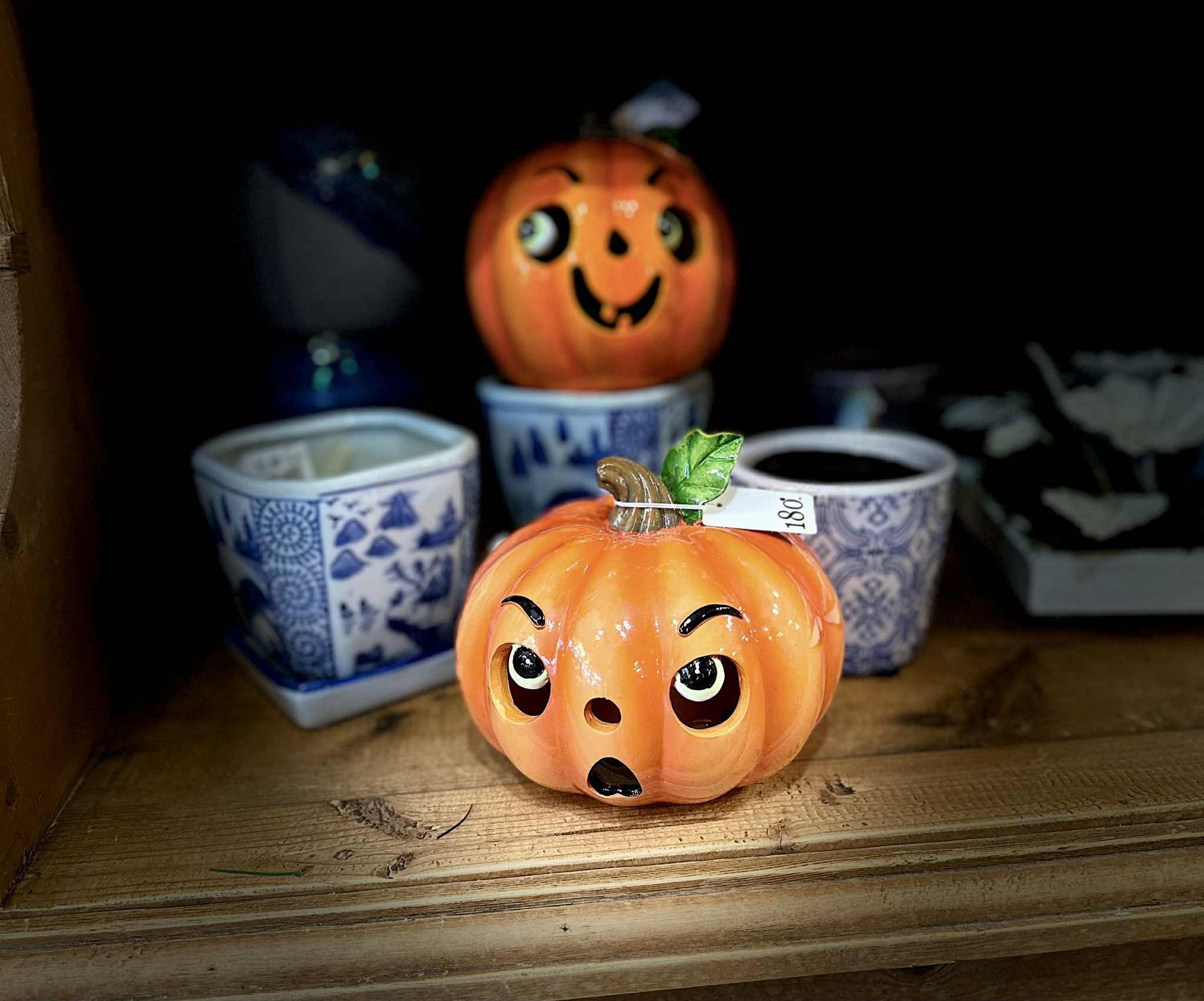 Ceramic pumpkins with surprised and happy faces on a shelf with decorative pots.