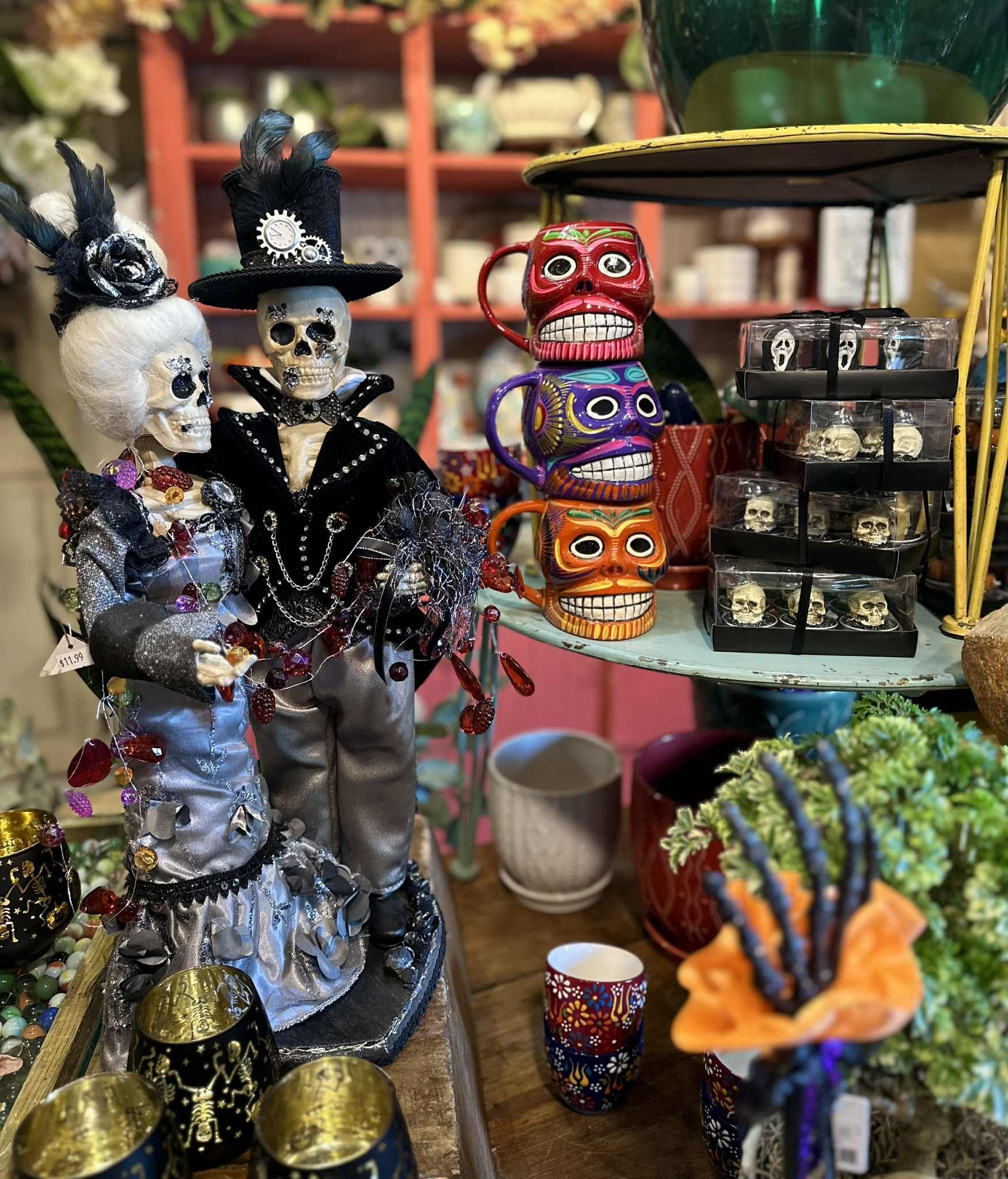 Dia de los Muertos display: Skeleton couple figurines, stacked colorful skull mugs, and decorative items.
