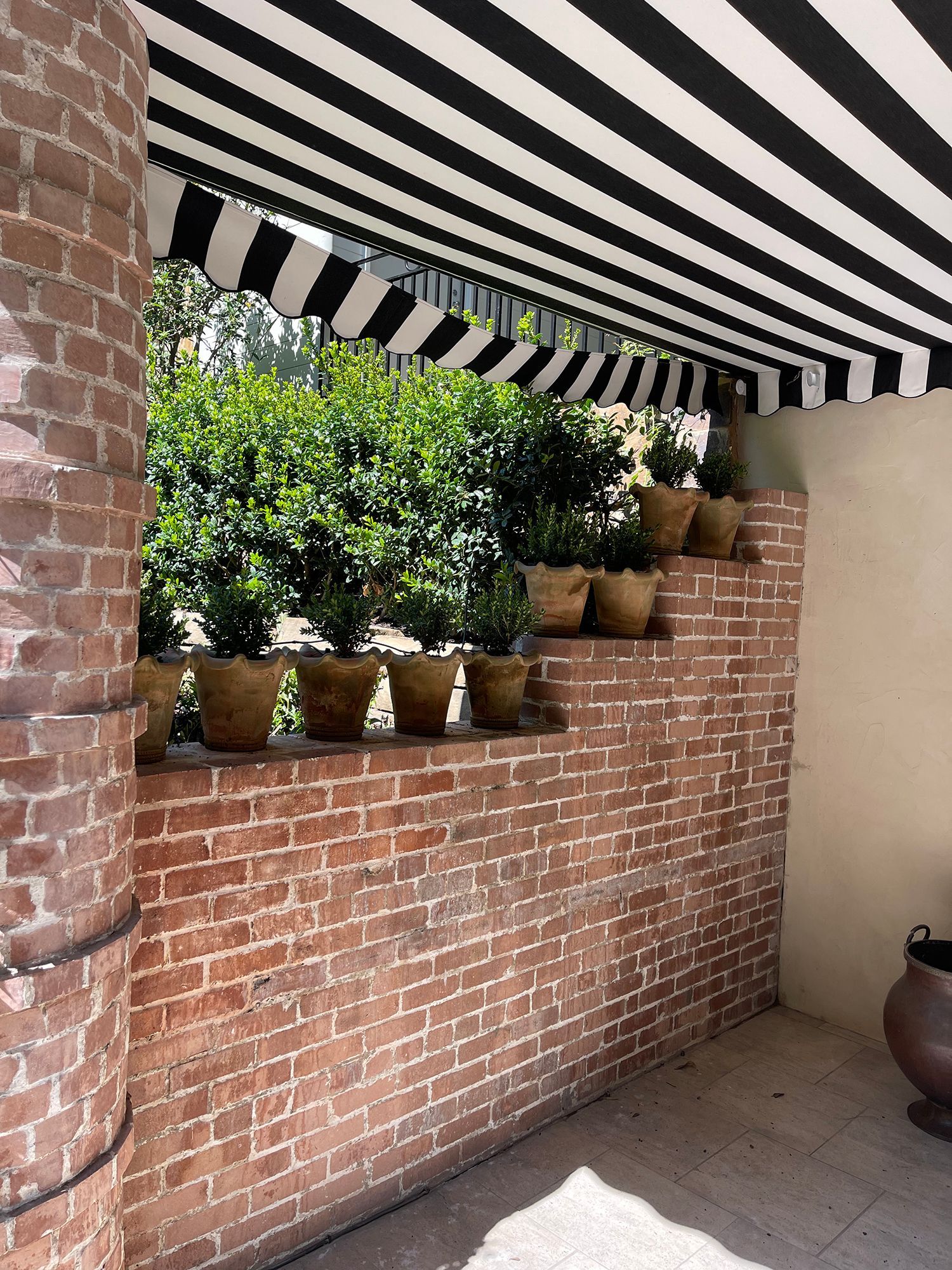 A brick wall with potted plants under a black and white striped awning.