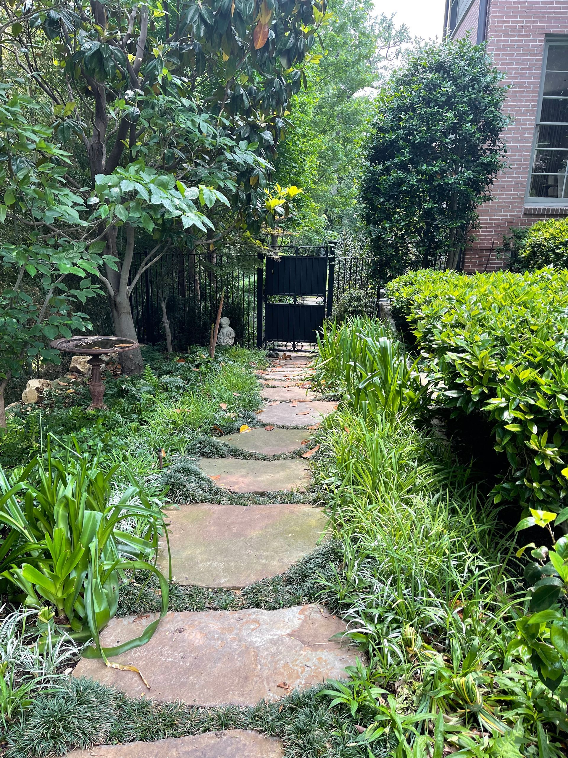 A stone path leading to a gate in a garden surrounded by trees and bushes.