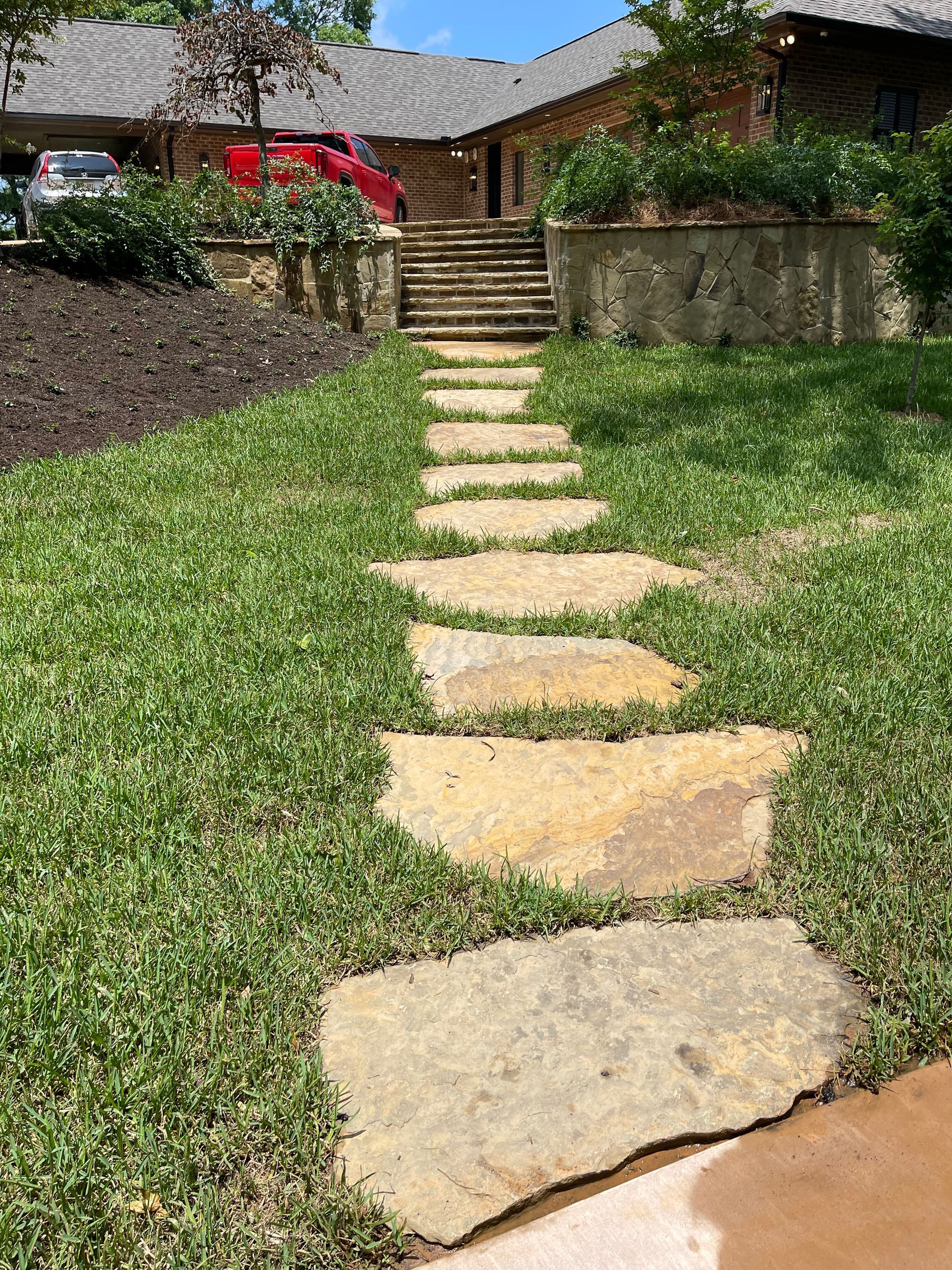 A stone walkway leading to a house on a lush green hillside.