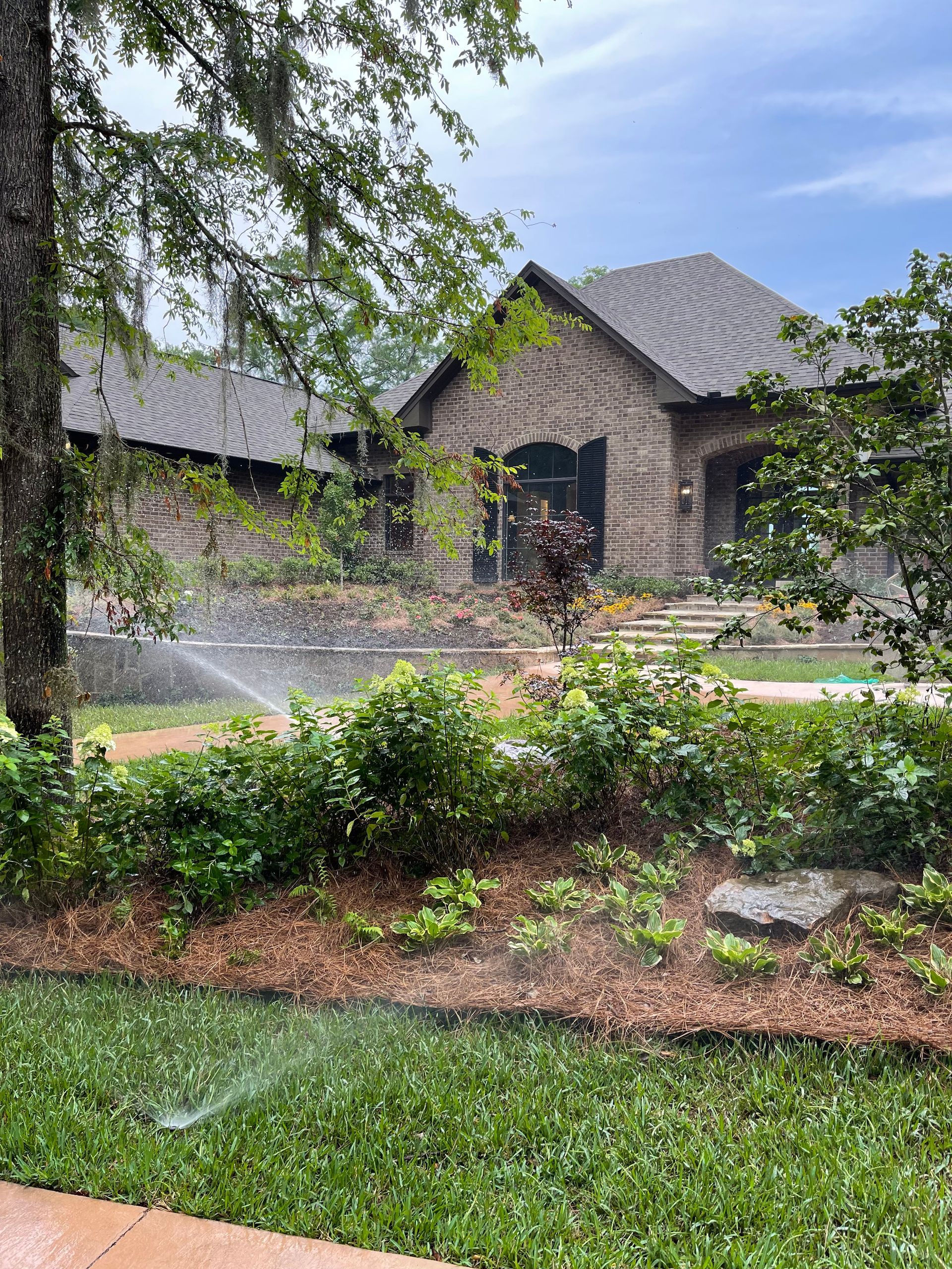 A sprinkler is spraying water on a lush green lawn in front of a large house.