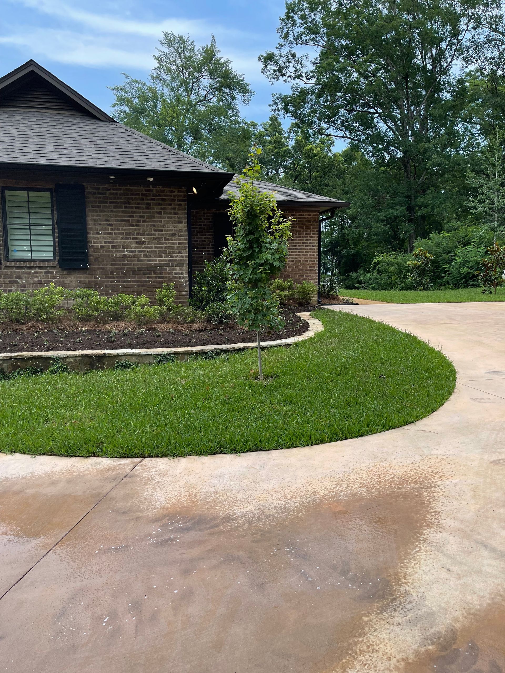 A brick house with a driveway and a lush green lawn in front of it.