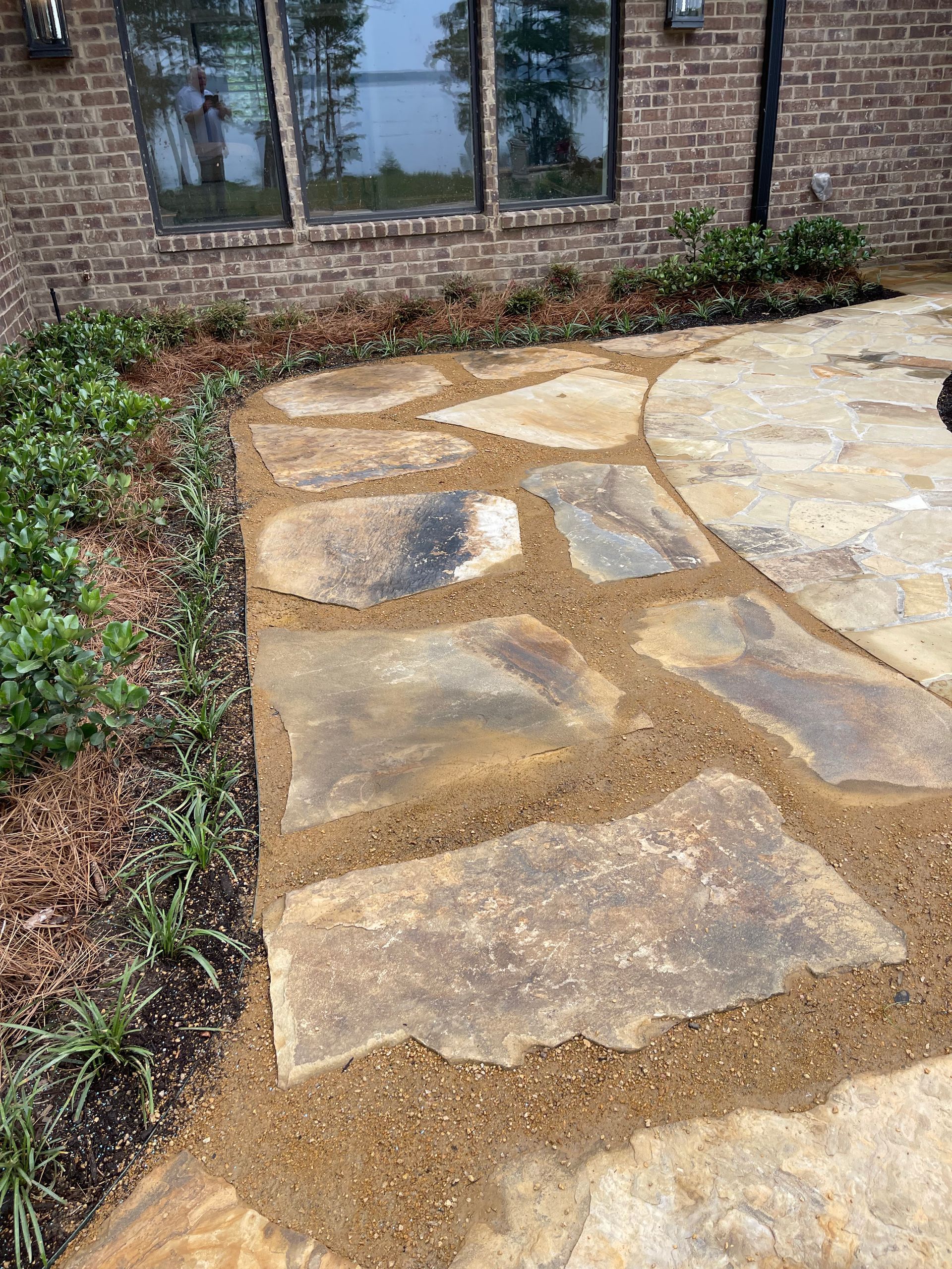 A stone walkway leading to a patio in front of a brick house.