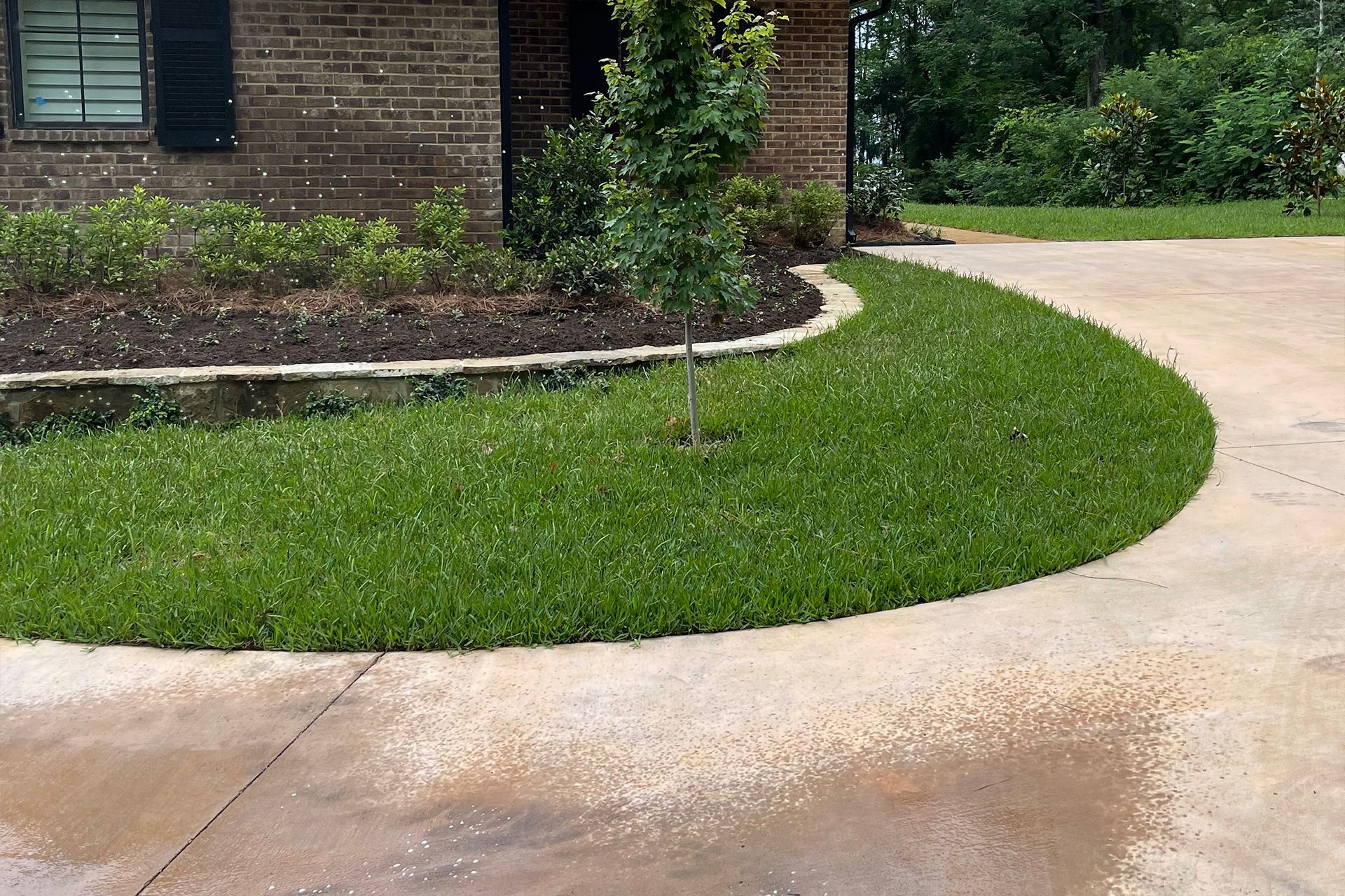 A brick house with a curved driveway and a lush green lawn in front of it.