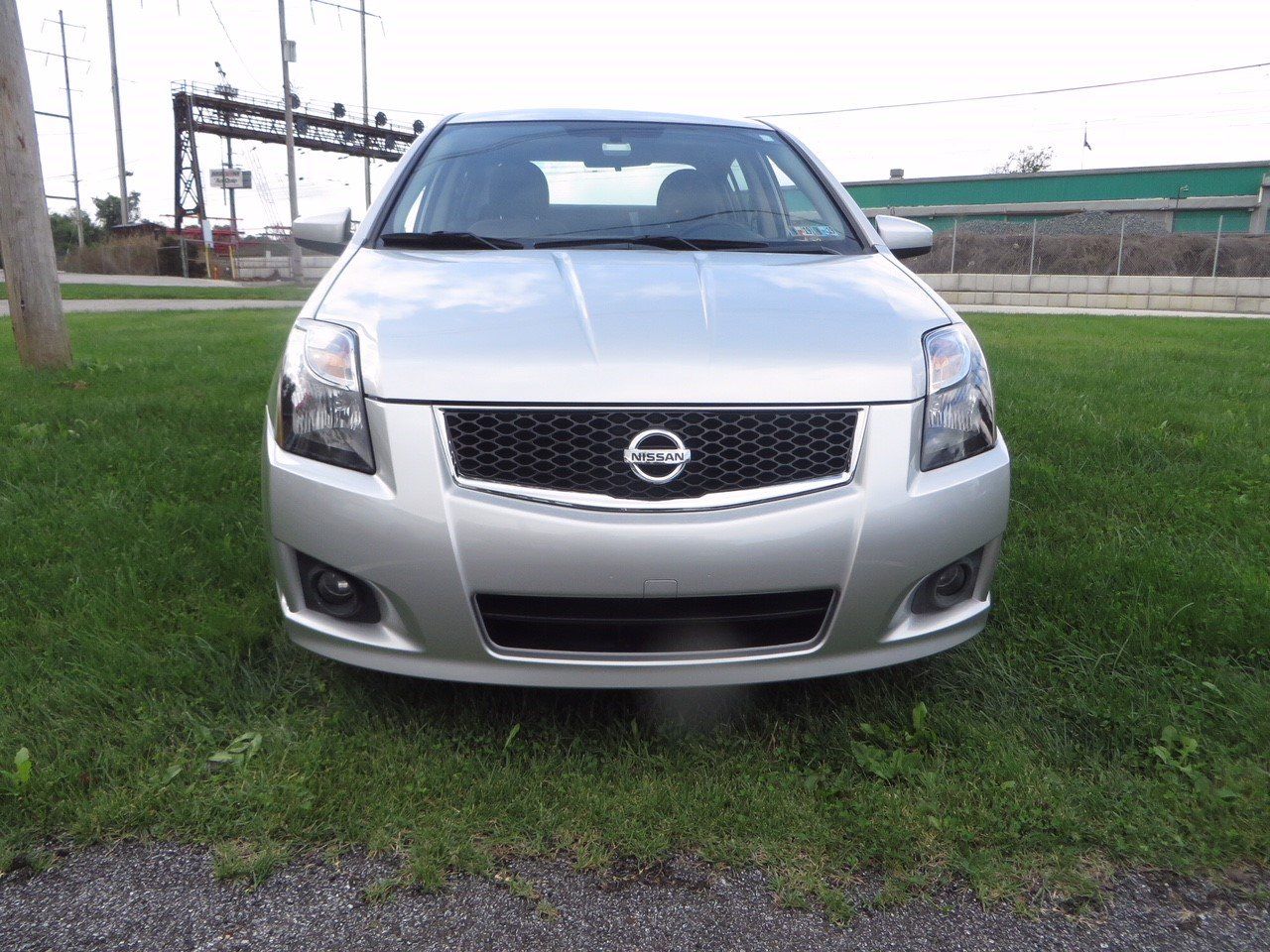 The front of a silver nissan sentra is parked in the grass.