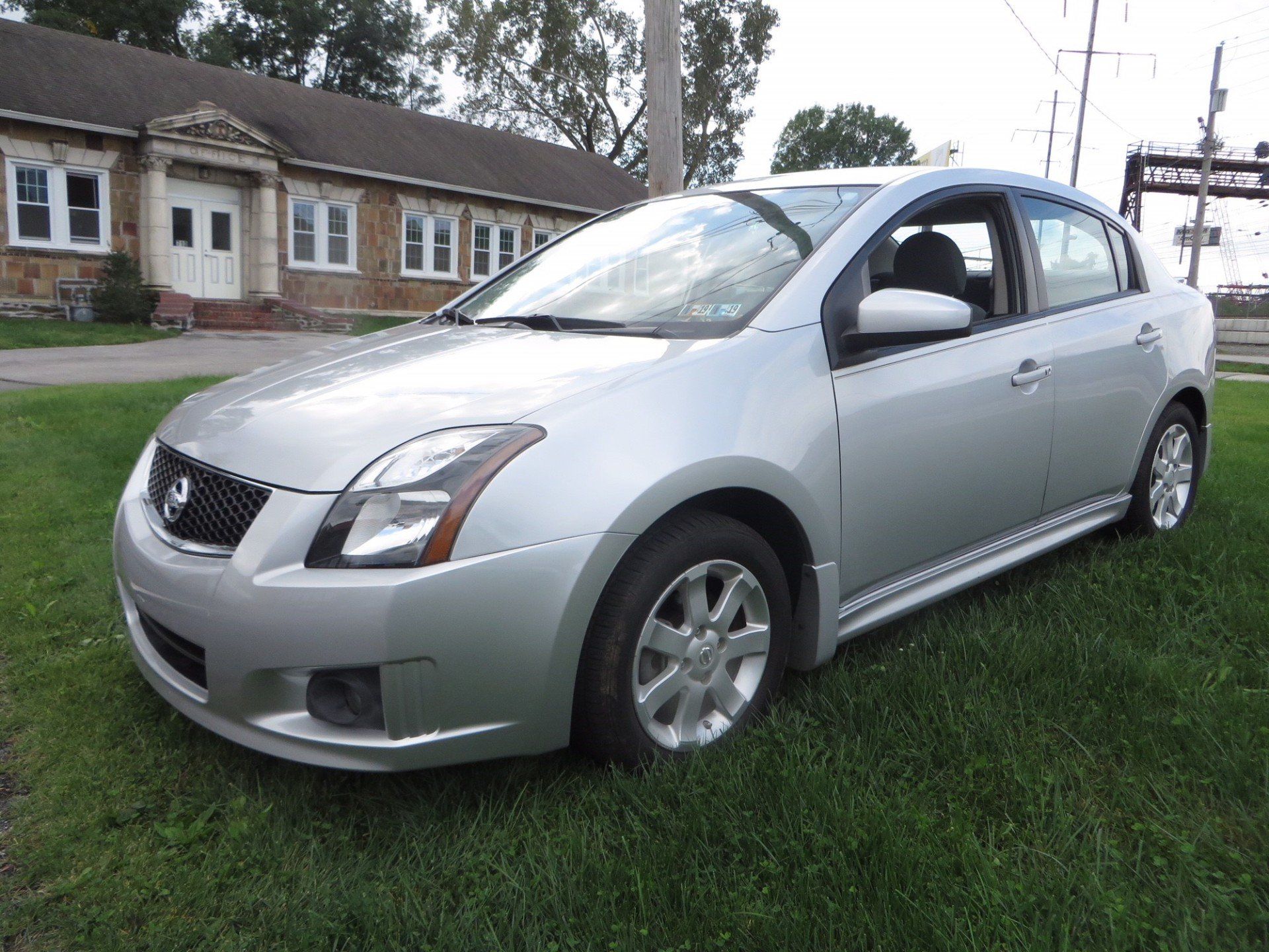 A silver car is parked in the grass in front of a building.