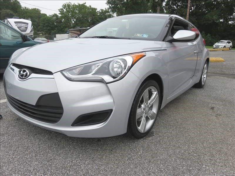 A silver hyundai veloster is parked in a parking lot.