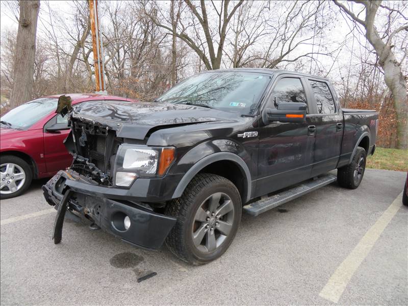 A black pickup truck with a damaged bumper is parked in a parking lot.
