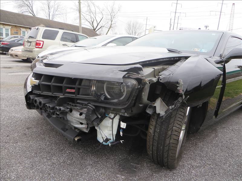 A black car with a damaged front end is parked in a parking lot.