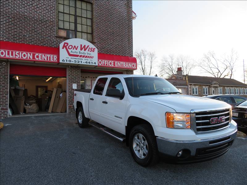 A white truck is parked in front of a ron wise collision center