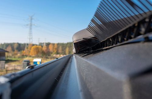 Low-angle view along a metal rooftop edge against blue sky and autumn trees