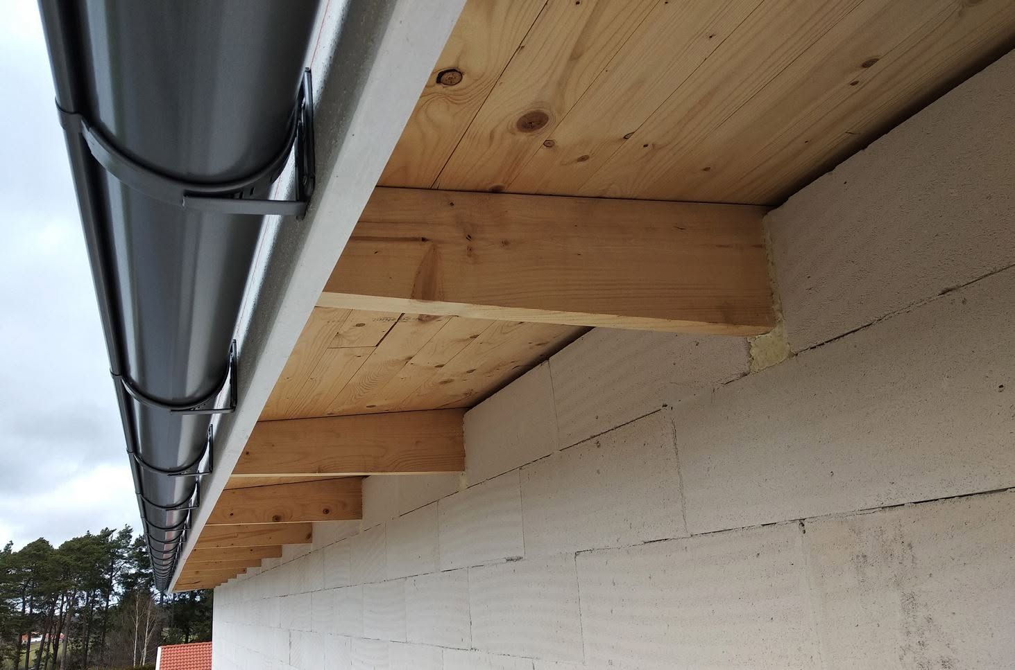 Close-up of wooden roof eaves and white exterior wall with exposed metal guttering