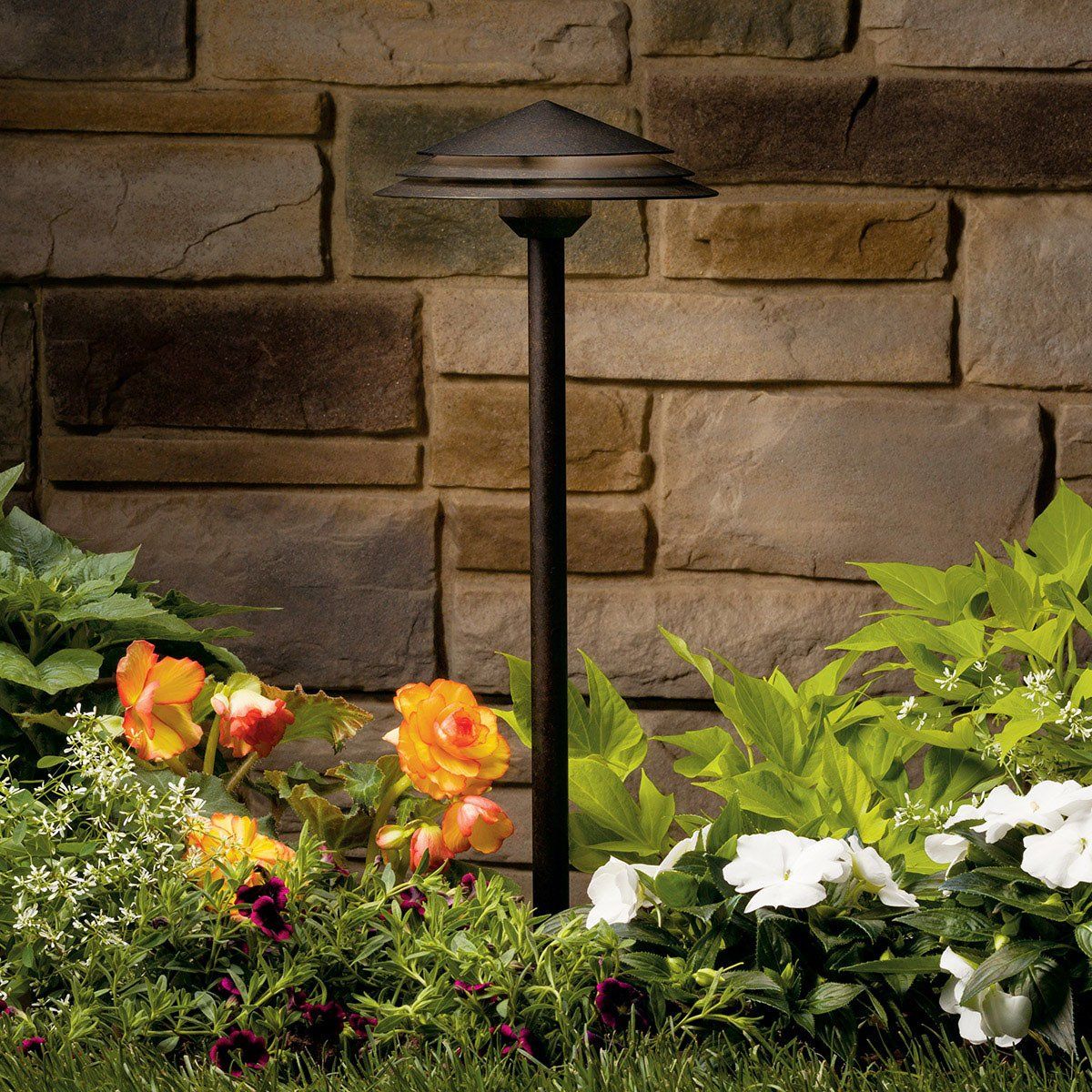 A garden with flowers and a lamp in front of a brick wall