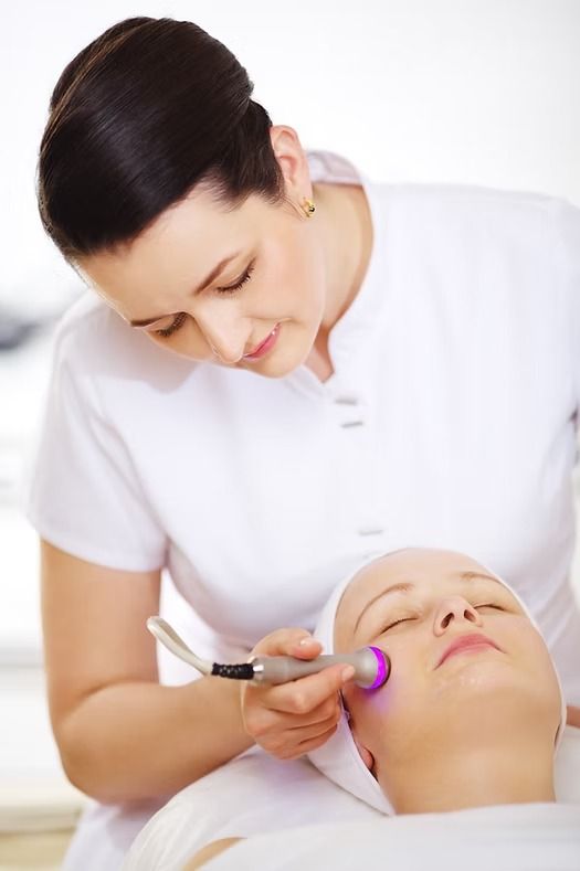 Cosmetologist applying facial treatment with a glowing device to a relaxed client lying down