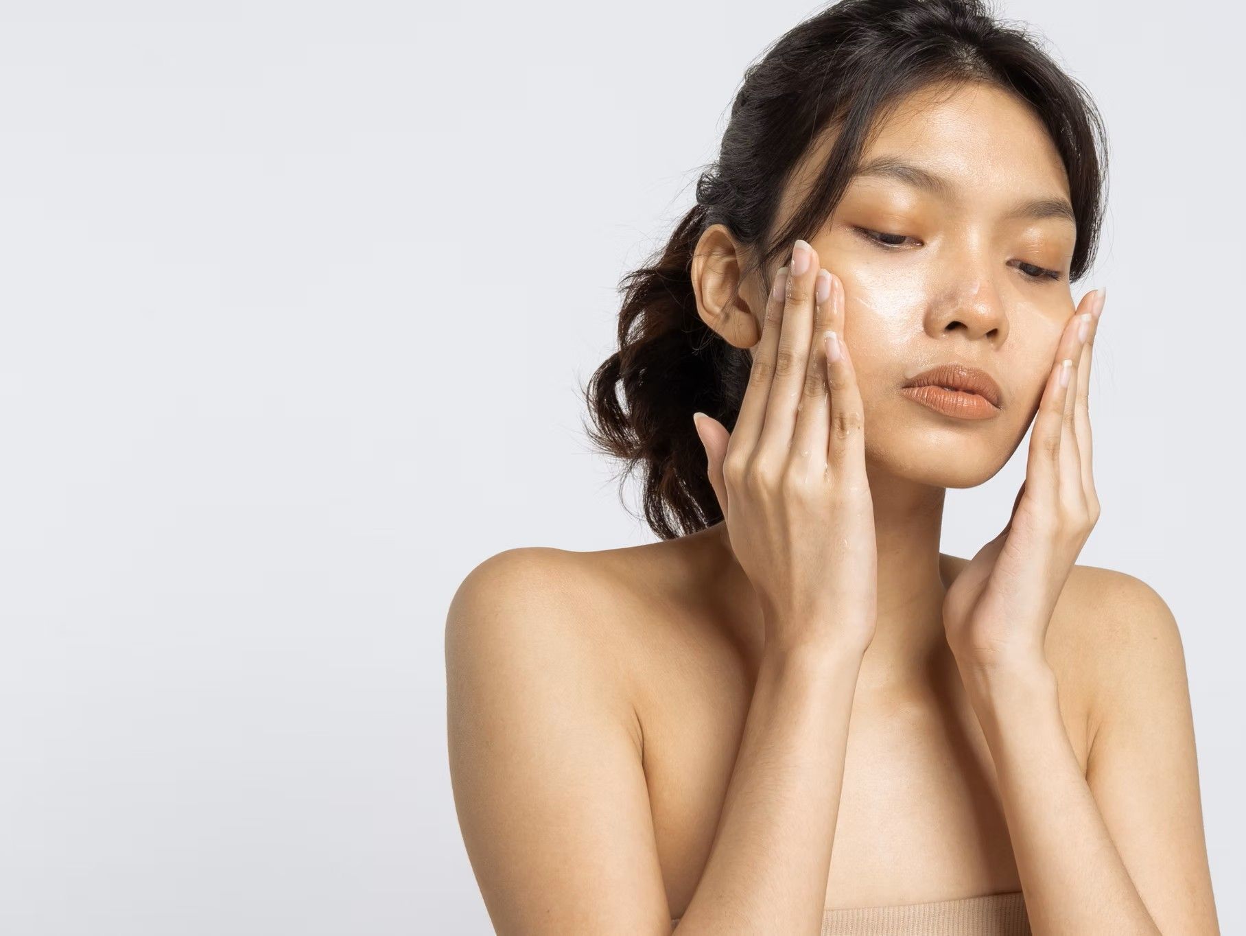 Woman gently touching her face with both hands against a light background