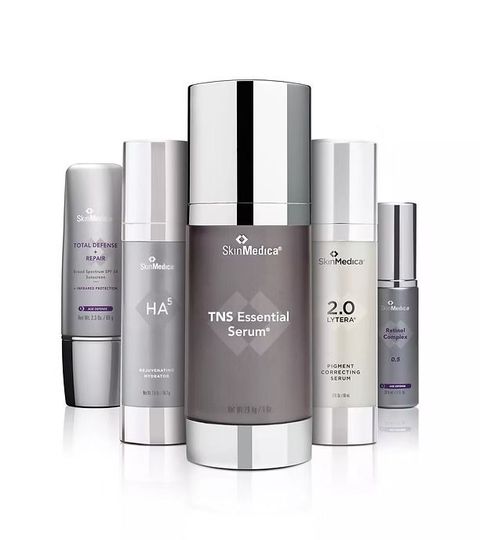 Skincare product bottles and jars arranged around a central silver serum bottle on a white background