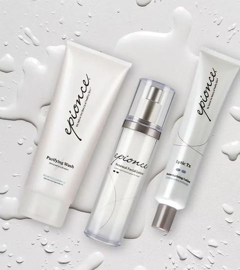 Three white skincare bottles and tubes on a wet white background