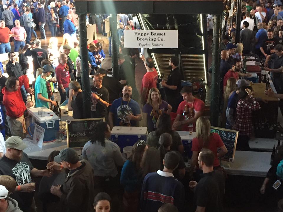 People gathered at the Happy Gnome Brewing Co. booth at an event, staff serving beer. Crowds and a dark, indoor setting.