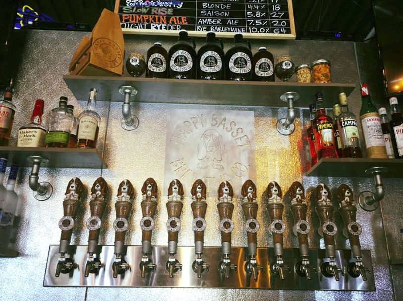 A bar with several beer taps, bottles, and a chalkboard menu above. The setting is dimly lit.