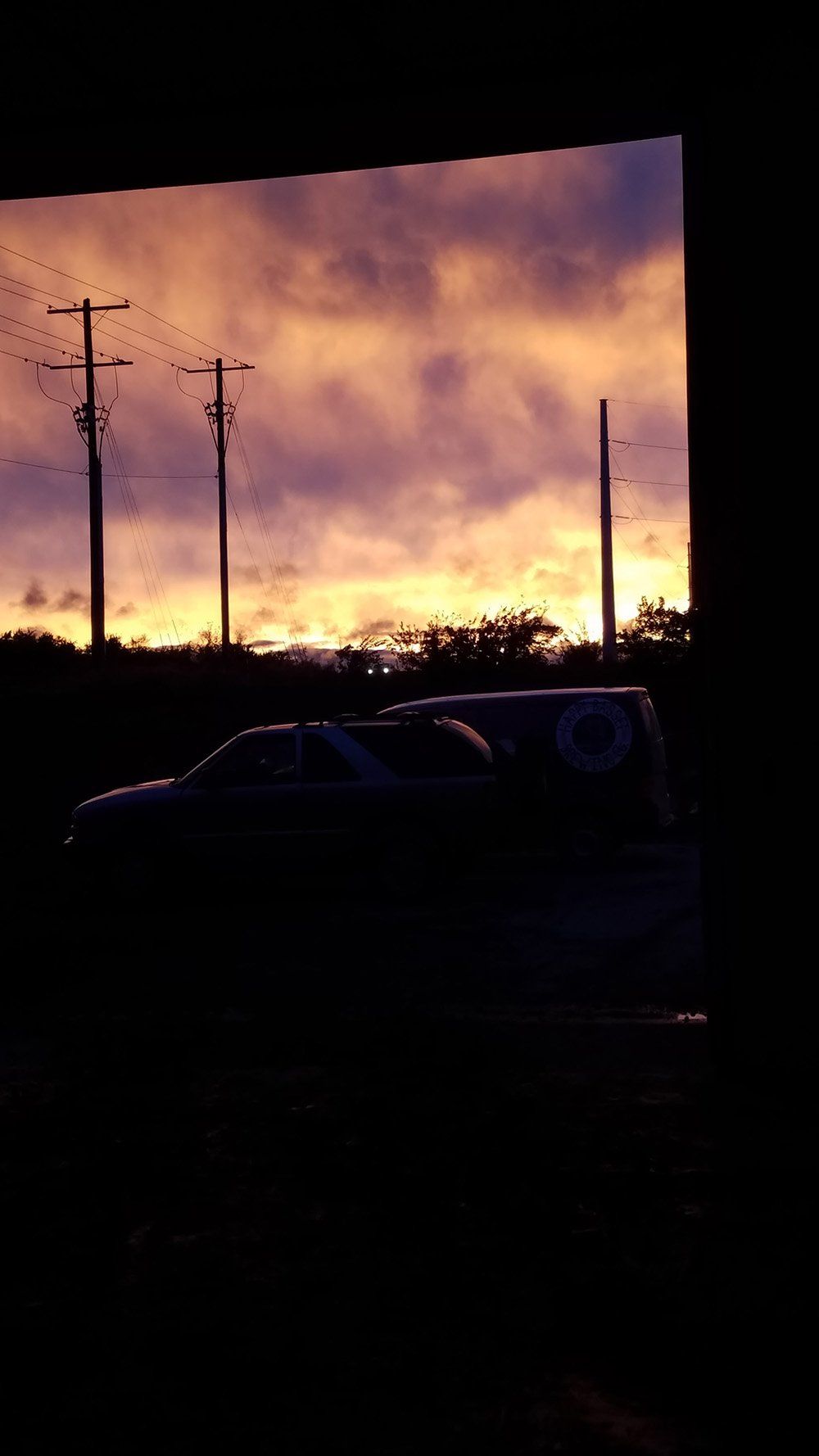 Sunset through a window, with power lines and silhouette of a vehicle. Orange and purple sky.