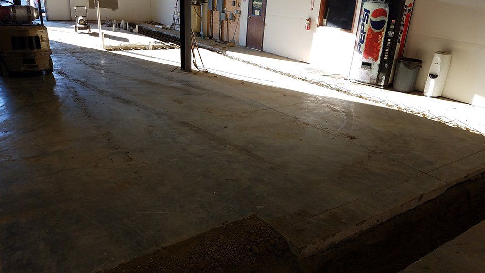 Interior shot of a concrete floor in a loading dock area, with a forklift, and some sunlight.