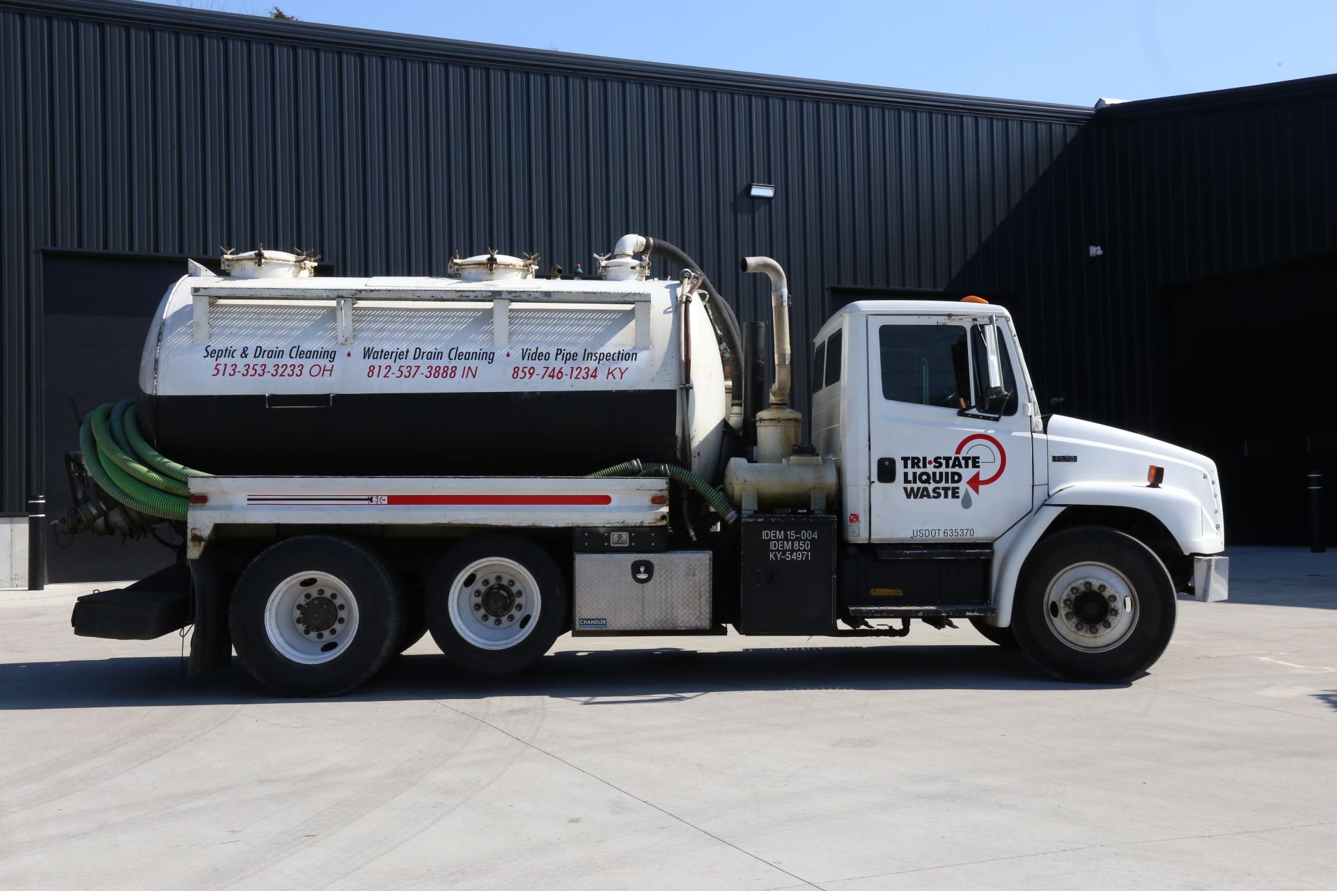 a white and black vacuum truck is parked in front of a building .