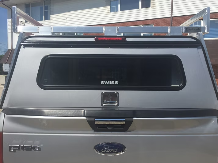 Silver truck bed with topper and roof rack, Ford logo. The topper has a rear window, and a lock.