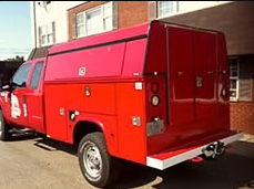 Red utility truck with a large enclosed bed, parked outside a building.