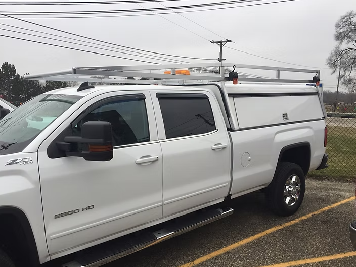 White pickup truck with a cap and roof rack, parked outside.