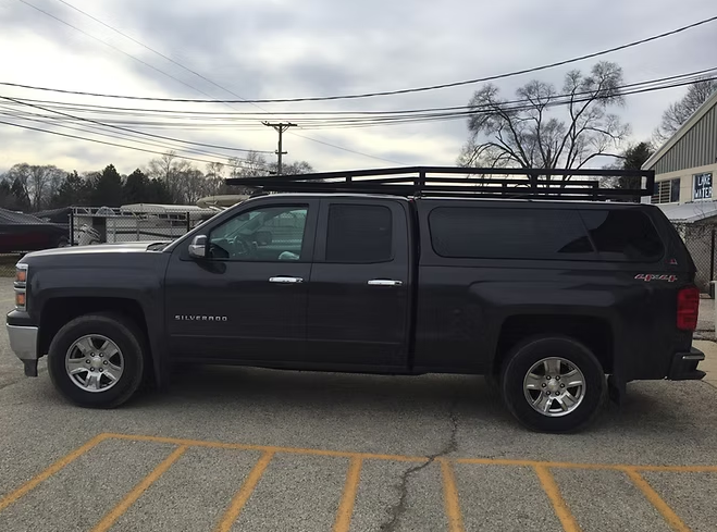 Dark gray Chevy Silverado truck with a black roof rack and camper shell parked outdoors.