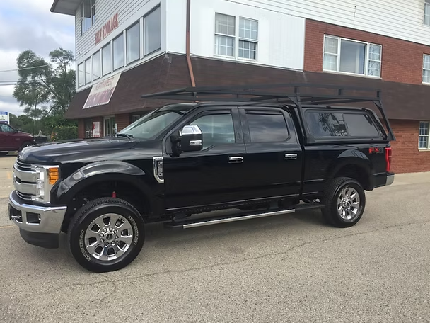 Black pickup truck with camper shell parked in front of a building.