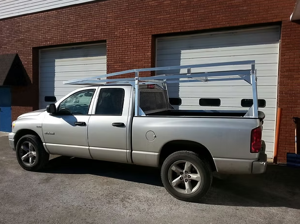 Silver pickup truck with a ladder rack parked outside a brick building with garage doors.