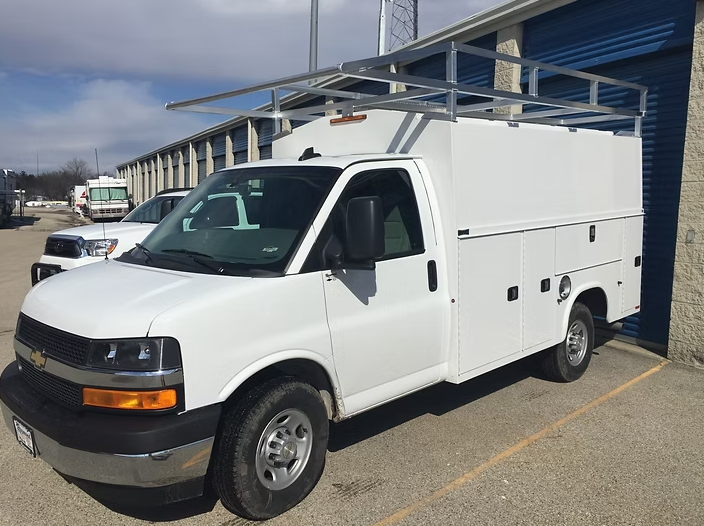 White work van with ladder rack parked outside a storage facility.