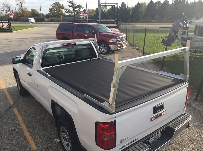 White pickup truck with a black tonneau cover and a wooden ladder rack.