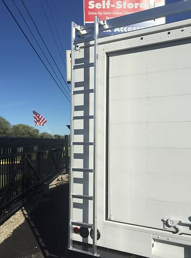 A white storage unit with a ladder on the side. An American flag flies in the background.