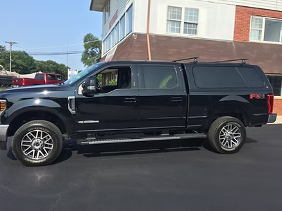 Black Ford F-series pickup truck with a black camper shell parked in front of a building.