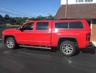 Red pickup truck with a camper shell parked outside a building on a sunny day.