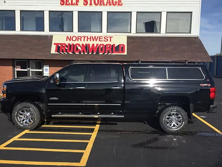 Black truck with camper shell parked in front of a Northwest Truckworld building with self storage.