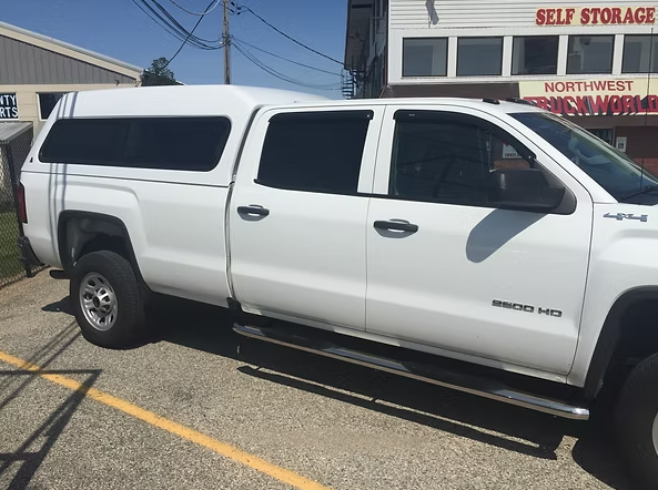 White pickup truck with a camper shell parked in front of a storage facility.