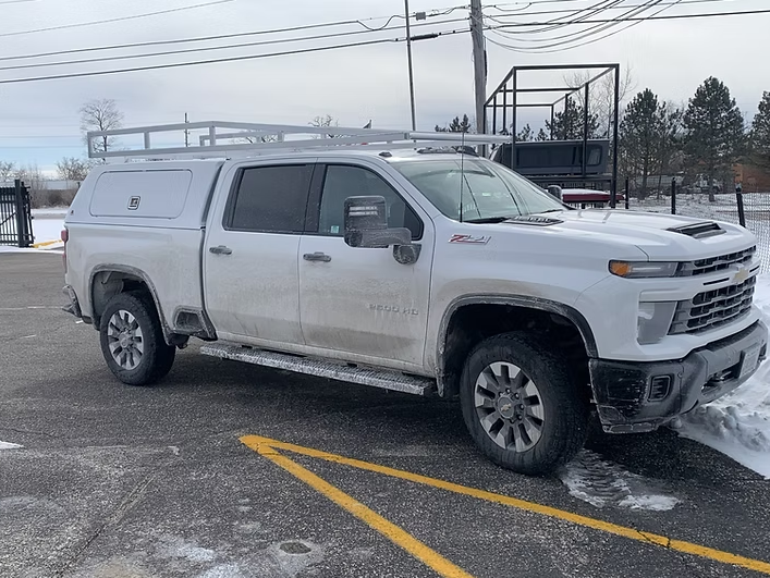 White Chevrolet truck with cap and roof rack parked in snowy lot.