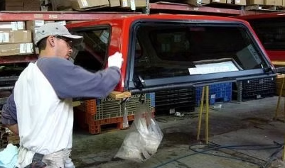 Man working on a red truck cap in a warehouse.