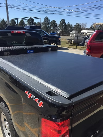 Black pickup truck bed with a closed black tonneau cover and a toolbox.