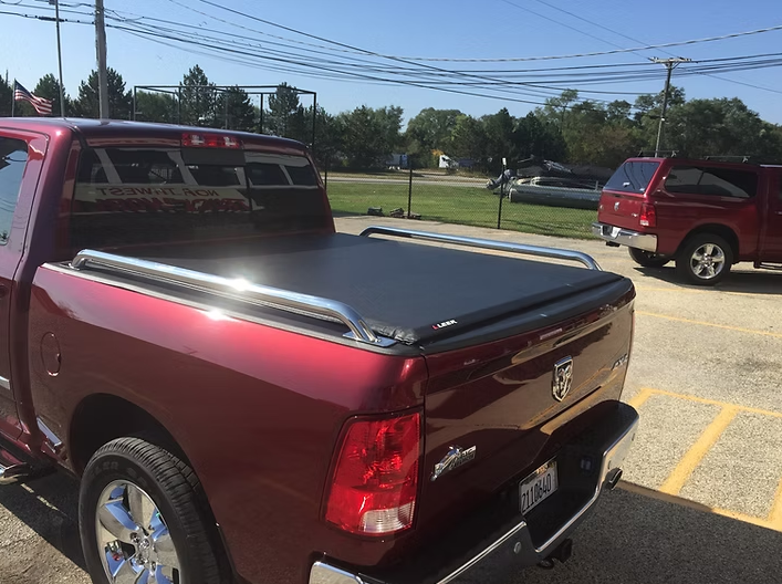 Red pickup truck with black tonneau cover and chrome bars parked outdoors.