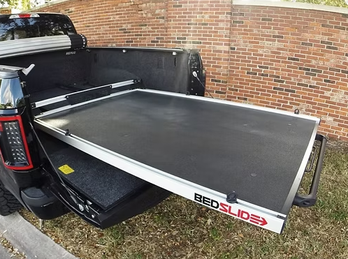 Black truck bed with a sliding bed slide extended, outdoors. White frame, black surface, 