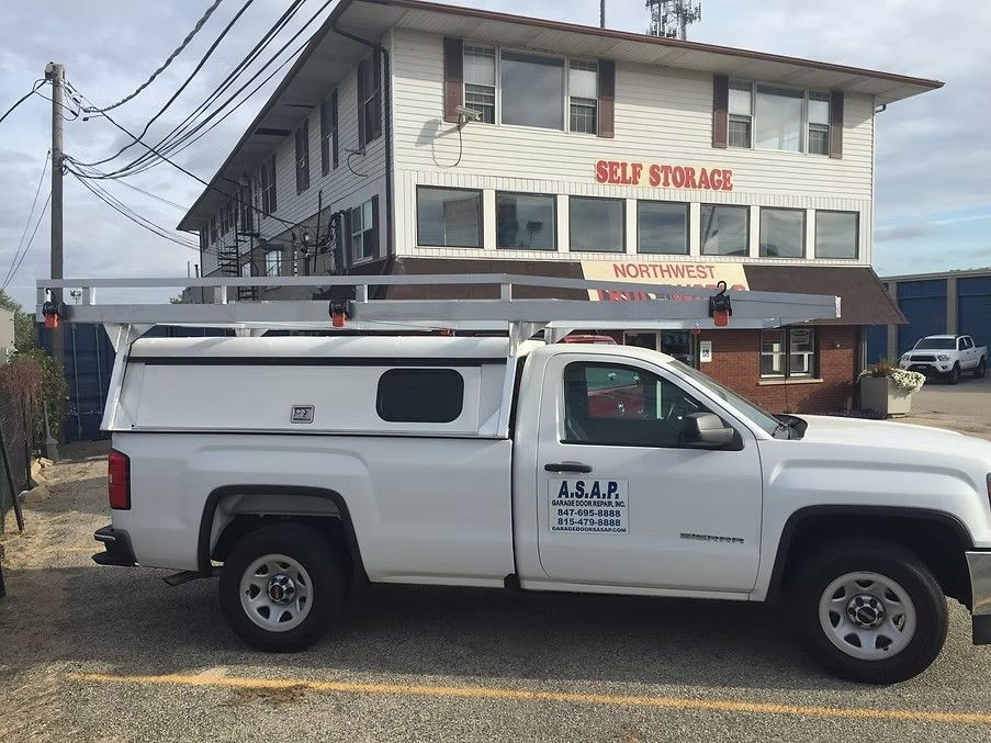 White pickup truck with ladder rack parked in front of a self-storage building.