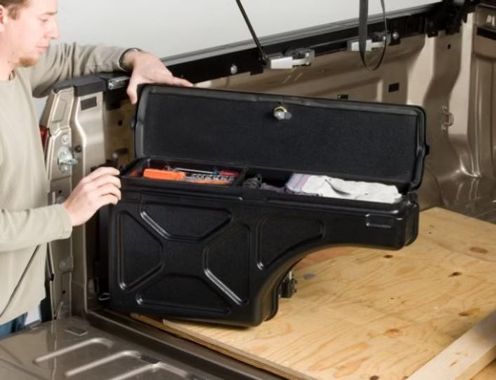 Man opening a black truck bed toolbox with tools and supplies.