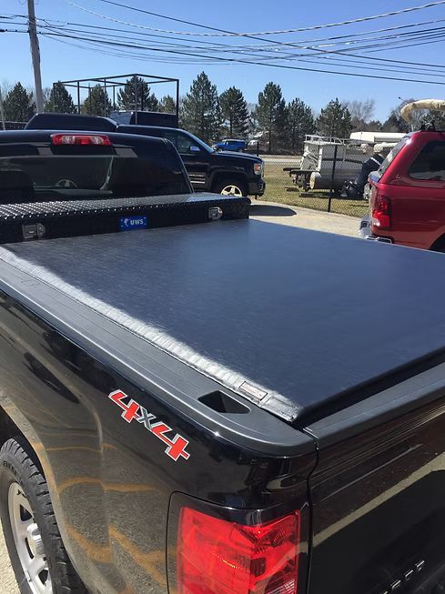 Black pickup truck bed cover with a diamond plate toolbox. 4x4 emblem visible.