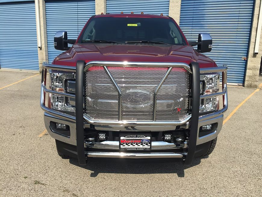 Red pickup truck with a large, chrome grill guard parked in front of closed blue garage doors.